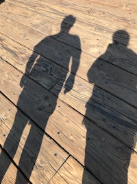 the shadows of two people standing on a wooden deck